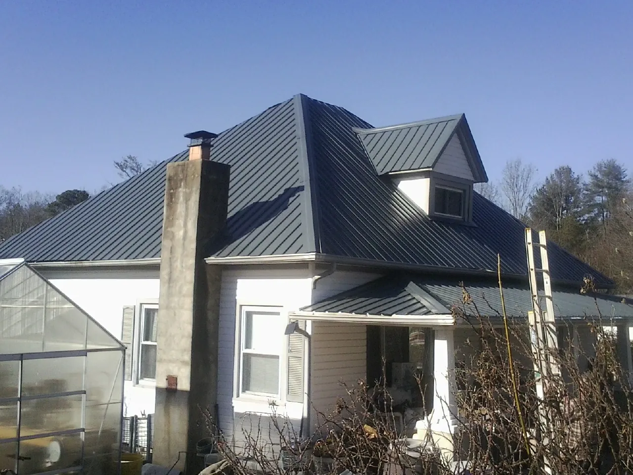 Dark blue standing seam metal roof on a white farmhouse with dormer — Slate & Tile Roof Repair by Roofing Brothers in Harrison