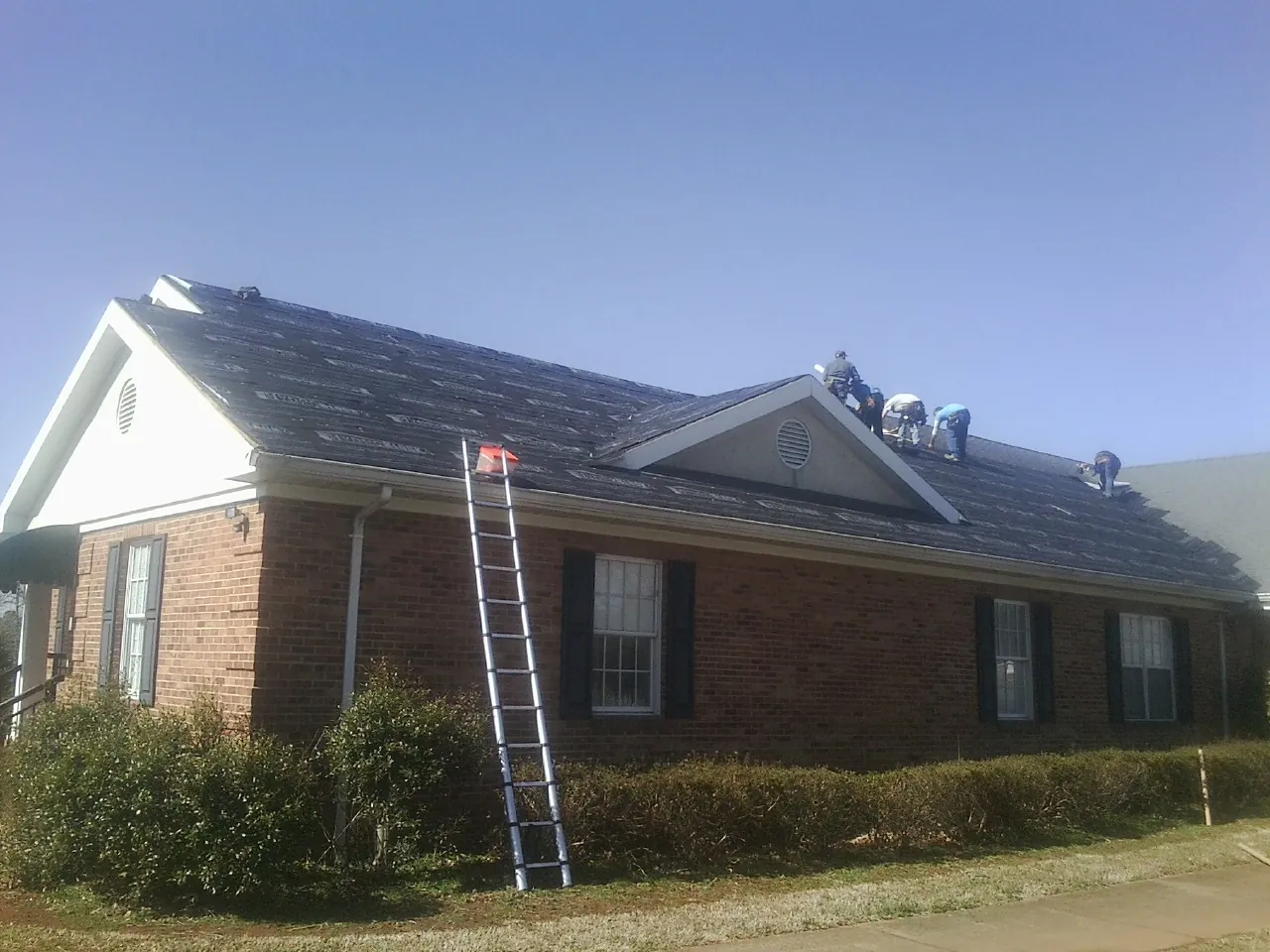Crew tearing shingles off a brick ranch roof with a ladder set — Emergency Roof Repair work by our crew in Harrison